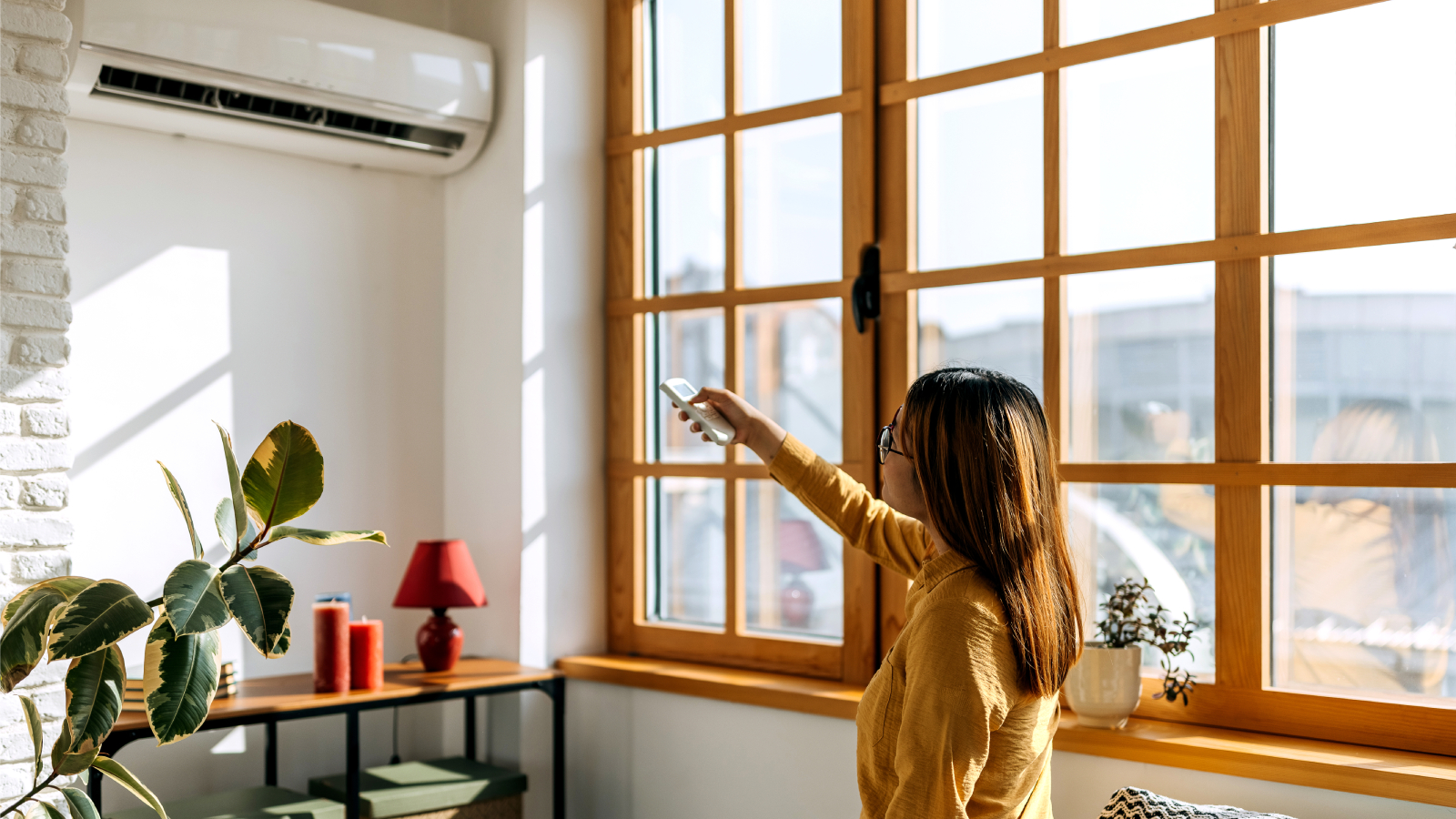 Relaxed young woman sitting on the couch and using the remote to change the room temperature of the ac unit