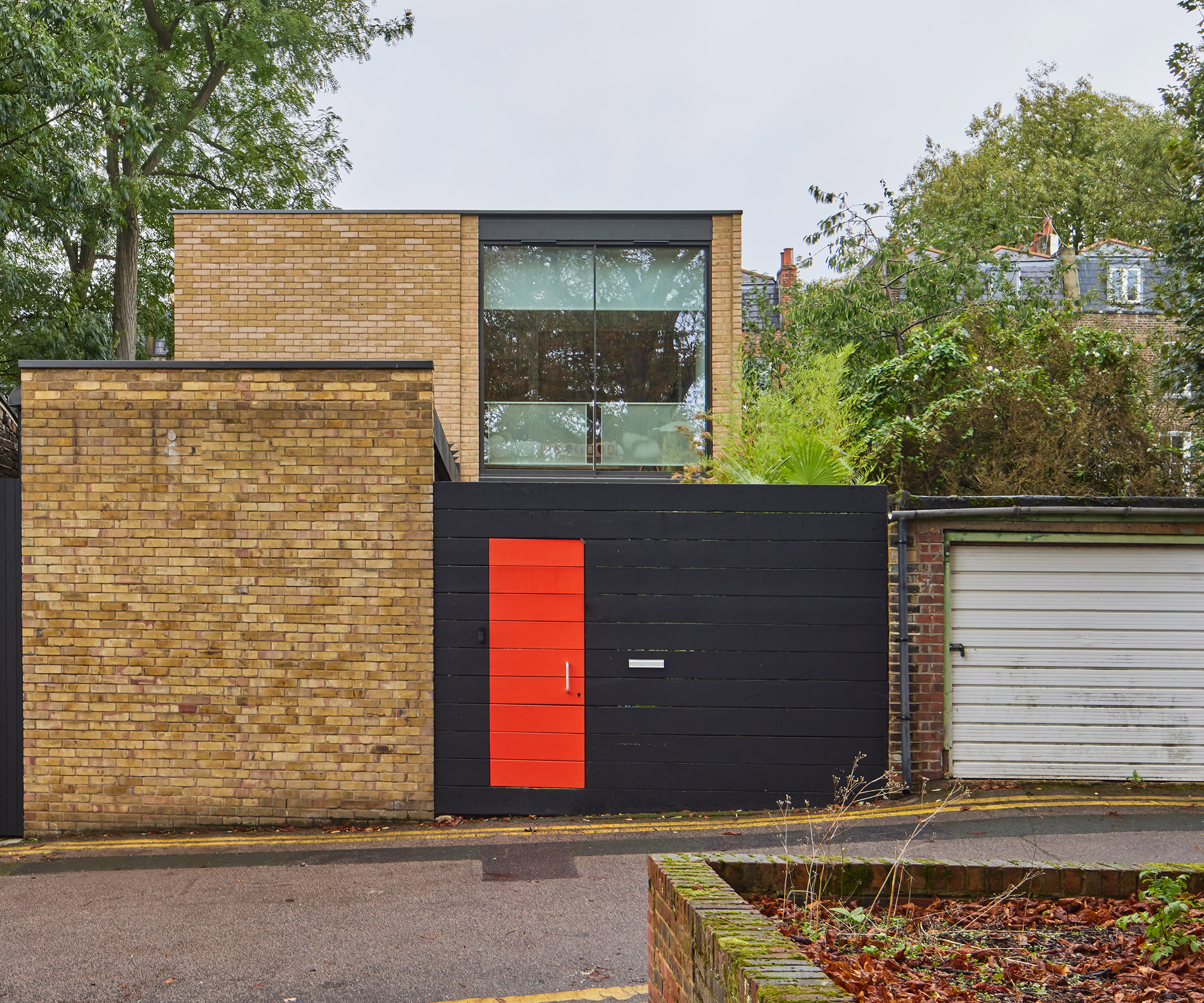 A contemporary home slotted amongst garages with a bright red door