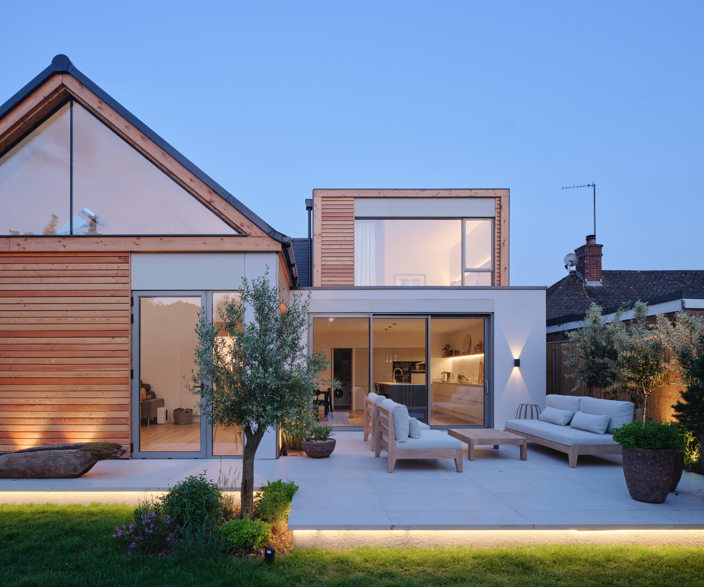 The rear of a contemporary bungalow renovation with soft exterior lighting and a paved patio area